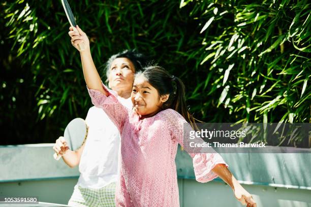 Young girl playing table tennis in backyard with aunt on sunny afternoon