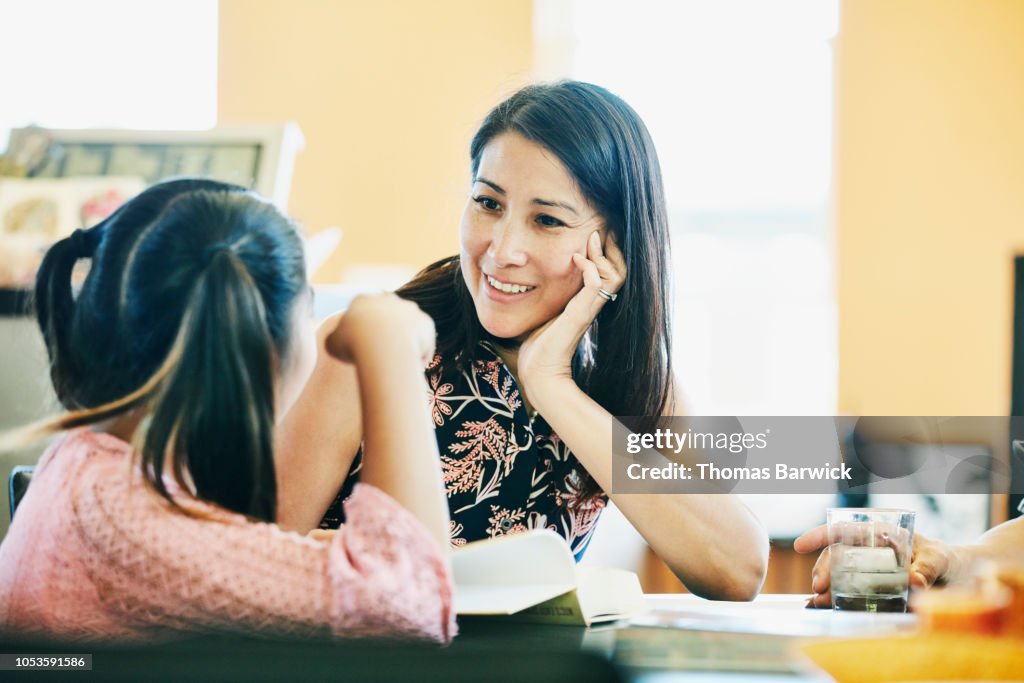 Smiling mother in discussion with daughter while doing homework in kitchen