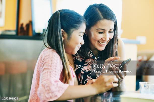 smiling mother and daughter making video call on smart phone at kitchen table - call us stockfoto's en -beelden