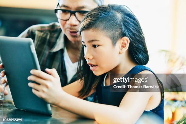 young girl looking at video on digital tablet with father at kitchen table - etnias asiáticas e indias - fotografias e filmes do acervo
