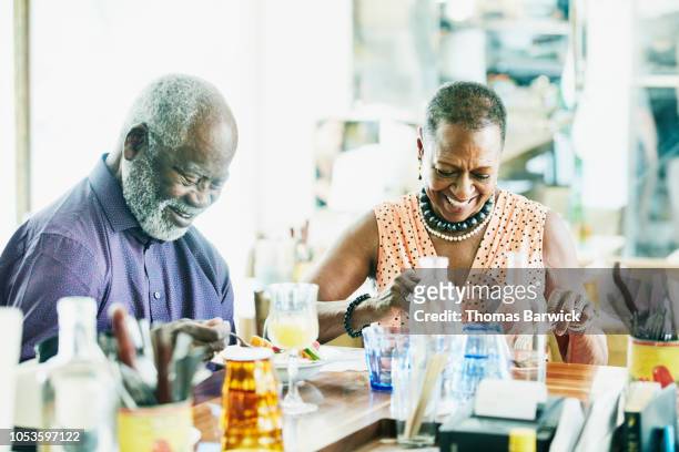laughing senior couple sharing lunch in restaurant on summer afternoon - old couple restaurant stock-fotos und bilder