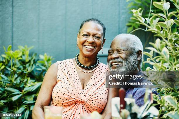 smiling senior woman sitting in husbands lap at outdoor cafe on summer afternoon - african american man helping elderly bildbanksfoton och bilder