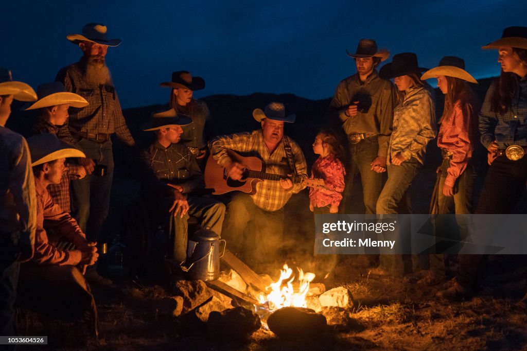 Large group of cowboys singing and playing guitar at campfire