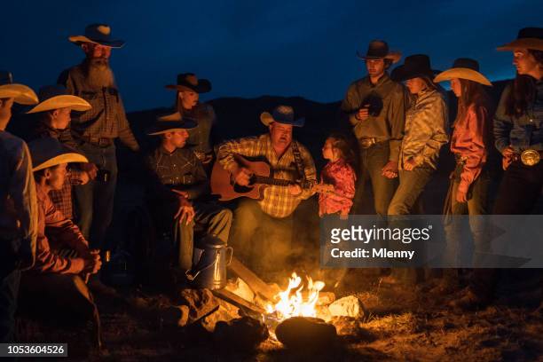 large group of cowboys singing and playing guitar at campfire - country and western music stock pictures, royalty-free photos & images