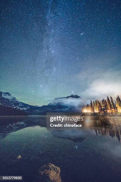emerald lake with illuminated cottage under milky way - star hotel stock pictures, royalty-free photos & images
