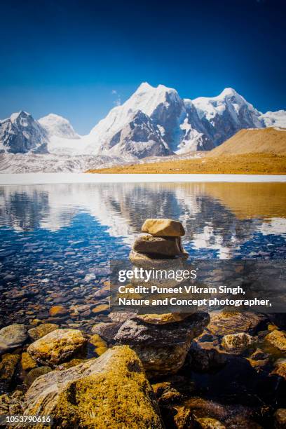 the partially frozen gurudongmar lake with stack of stones in foreground - northeast india stock pictures, royalty-free photos & images