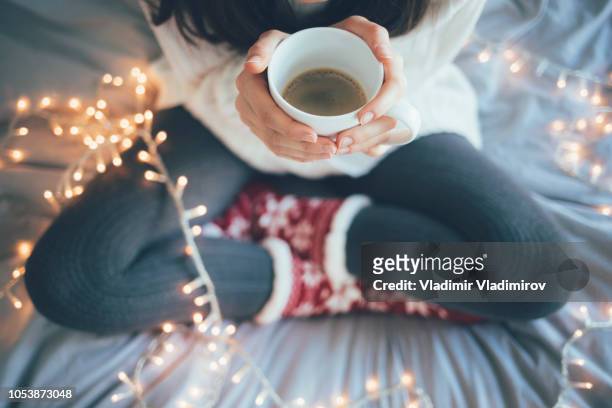 woman sitting legs crossed on bed and holding a cup - cosy stock pictures, royalty-free photos & images