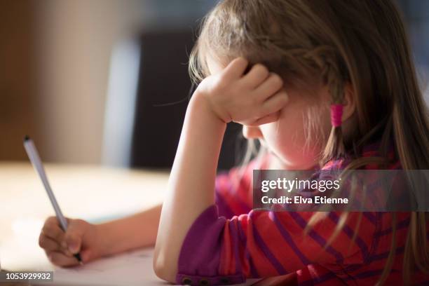 girl (6-7) leaning on elbows and drawing on a sketch pad on a table - young girls homework stock-fotos und bilder