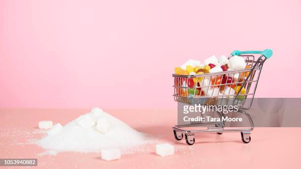 supermarket trolley with candy next to pile of sugar - sugar ストックフォトと画像