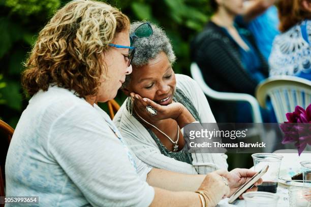 smiling friends looking at smart phone during backyard dinner party - 50 59 years stock pictures, royalty-free photos & images