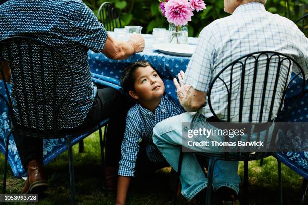 smiling young boy playing under table during family dinner party in backyard - party under stock pictures, royalty-free photos & images