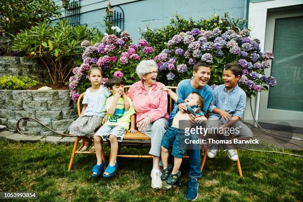 Laughing great grandmother and great grandchildren sitting in backyard garden