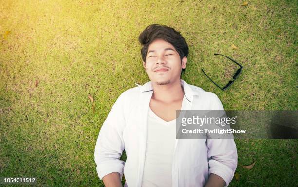 handsome man lying on the grass with happiness - sunglasses overhead stock pictures, royalty-free photos & images