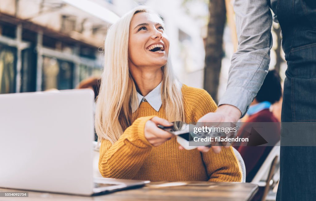 Schöne blonde Frau mit Smartphone Kontaktlos bezahlen