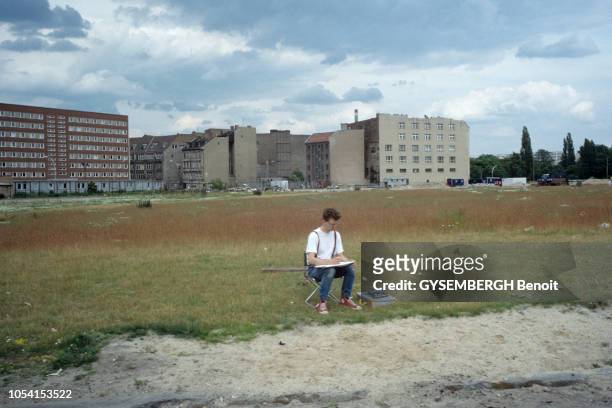 Vues de Berlin en juin 1991. Un jeune homme assis sur une chaise pliante, dessinant seul au milieu d'un terrain vague. A l'arrière plan, un ensemble...