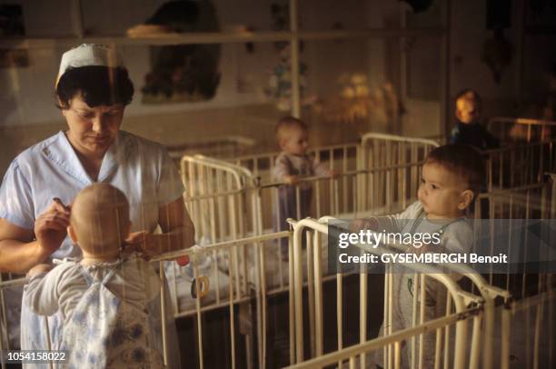 Les orphelinats de Roumanie. Octobre 1992. Femme donnant à manger à un bébé debout dans son lit à barreaux.