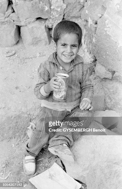 Yémen du Nord, juin 1977 --- Un petit garçon, assis dans la rue, jouant avec une canette de bière.