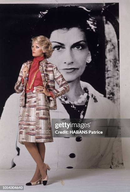 Devant le portrait géant noir et blanc de COCO CHANEL, un mannequin présente un tailleur Chanel de l'hiver 71.