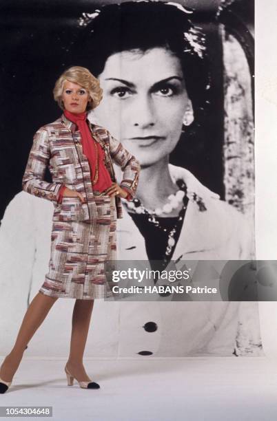 Devant le portrait géant noir et blanc de COCO CHANEL, un mannequin présente un tailleur Chanel de l'hiver 71.