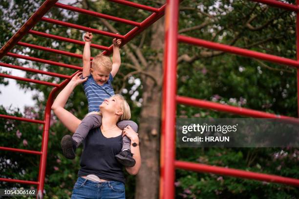 woman carrying son on shoulders below monkey bars - climbing frame stock pictures, royalty-free photos & images