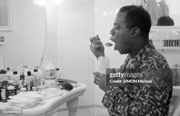 France, novembre 1955 --- Le trompettiste de jazz américain Louis ARMSTRONG en tournée en France. Dans une salle de bain devant le miroir, portant...