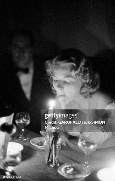 Le 9ème Festival de CANNES 1956 s'est déroulé du 23 avril au 10 mai : Ingrid BERGMAN allumant sa cigarette à la flamme d'une bougie, assise aux côtés...