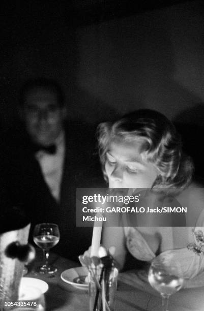 Le 9ème Festival de CANNES 1956 s'est déroulé du 23 avril au 10 mai : Ingrid BERGMAN allumant sa cigarette à la flamme d'une bougie, assise aux côtés...
