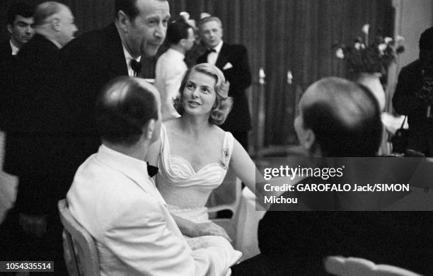 Le 9ème Festival de CANNES 1956 s'est déroulé du 23 avril au 10 mai : Georges SIMENON discutant debout à une table où sont assis Ingrid BERGMAN, son...