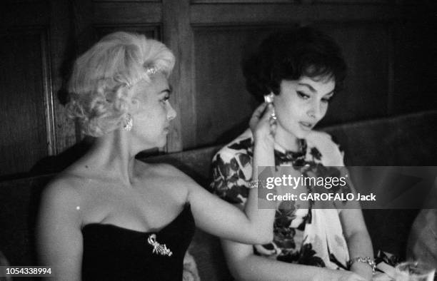 Le 11ème Festival de CANNES se déroule du 2 au 18 mai : Martine CAROL regardant la boucle d'oreille que porte Gina LOLLOBRIGIDA, toutes deux assises...