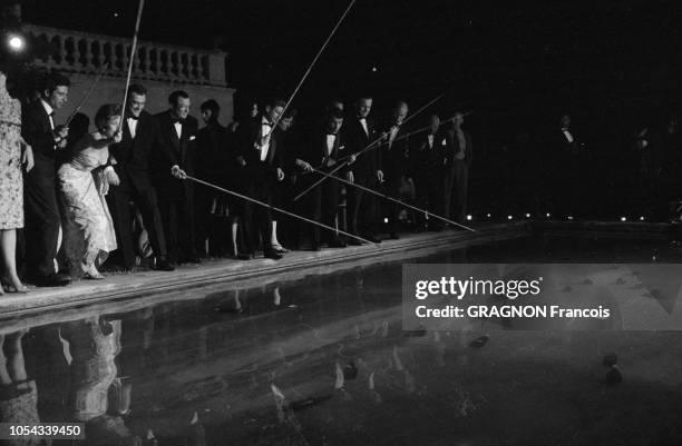 Le 13ème Festival de Cannes se déroule du 4 au 20 mai 1960 : soirée autour d'une piscine, les invités dont Gilbert BECAUD tenant un long bâton pour...