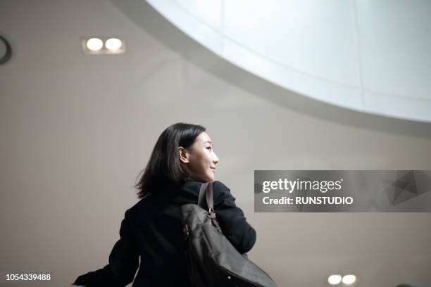 businesswoman standing on escalator - walking up stairs stockfoto's en -beelden