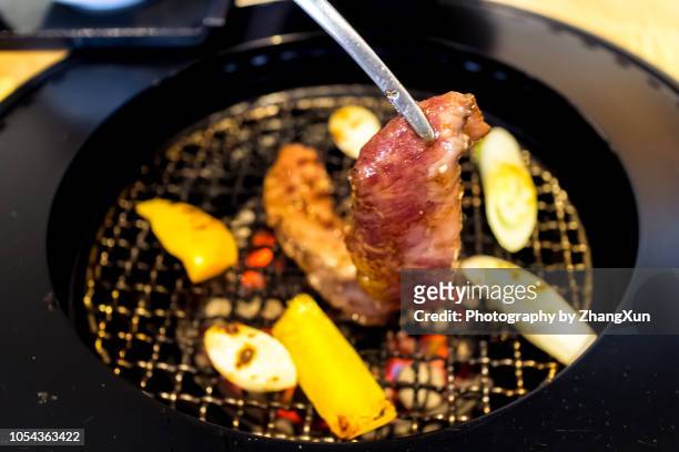 cropped image of people holding serving tongs over yakiniku on barbecue grill - yakiniku - fotografias e filmes do acervo