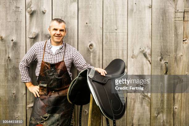 a saddle maker with one of his handmade saddles. - saddler stock pictures, royalty-free photos & images