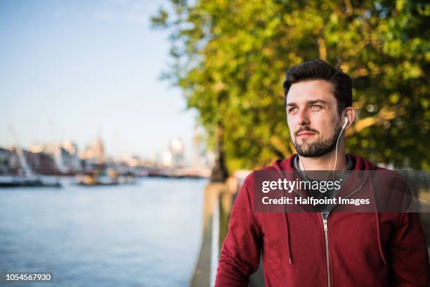 young sporty man with earphones standing on river promenade outside in a london city, listening to music. - england slovakia stock pictures, royalty-free photos & images