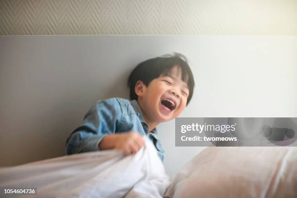 playful young boy rolling in bed. - boys jumping stock pictures, royalty-free photos & images