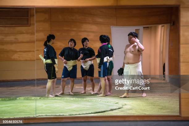Male university sumo wrestler walks past as members of the Asahi University women's sumo team chat ahead of a training session at the university sumo...