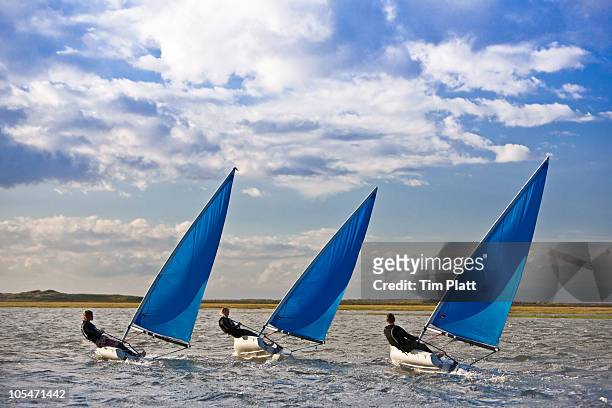 three dinghy sailors racing together. - triple stock pictures, royalty-free photos & images
