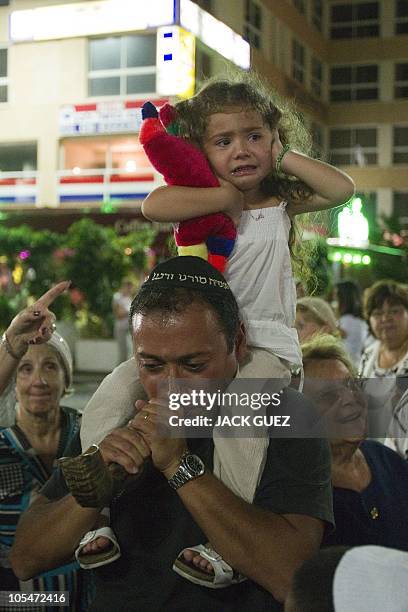 Young child covers her ears as a Jewish man blows a 'Shofar' horn during the Simhat Torah celebration in the coastal city of Netanya, north of Tel...