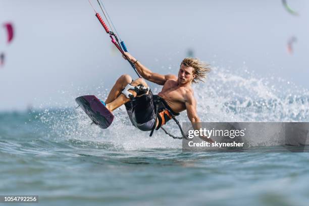 junger sportlicher mann spaß beim berühren des meeres während kiteboarding. - kite surf stock-fotos und bilder