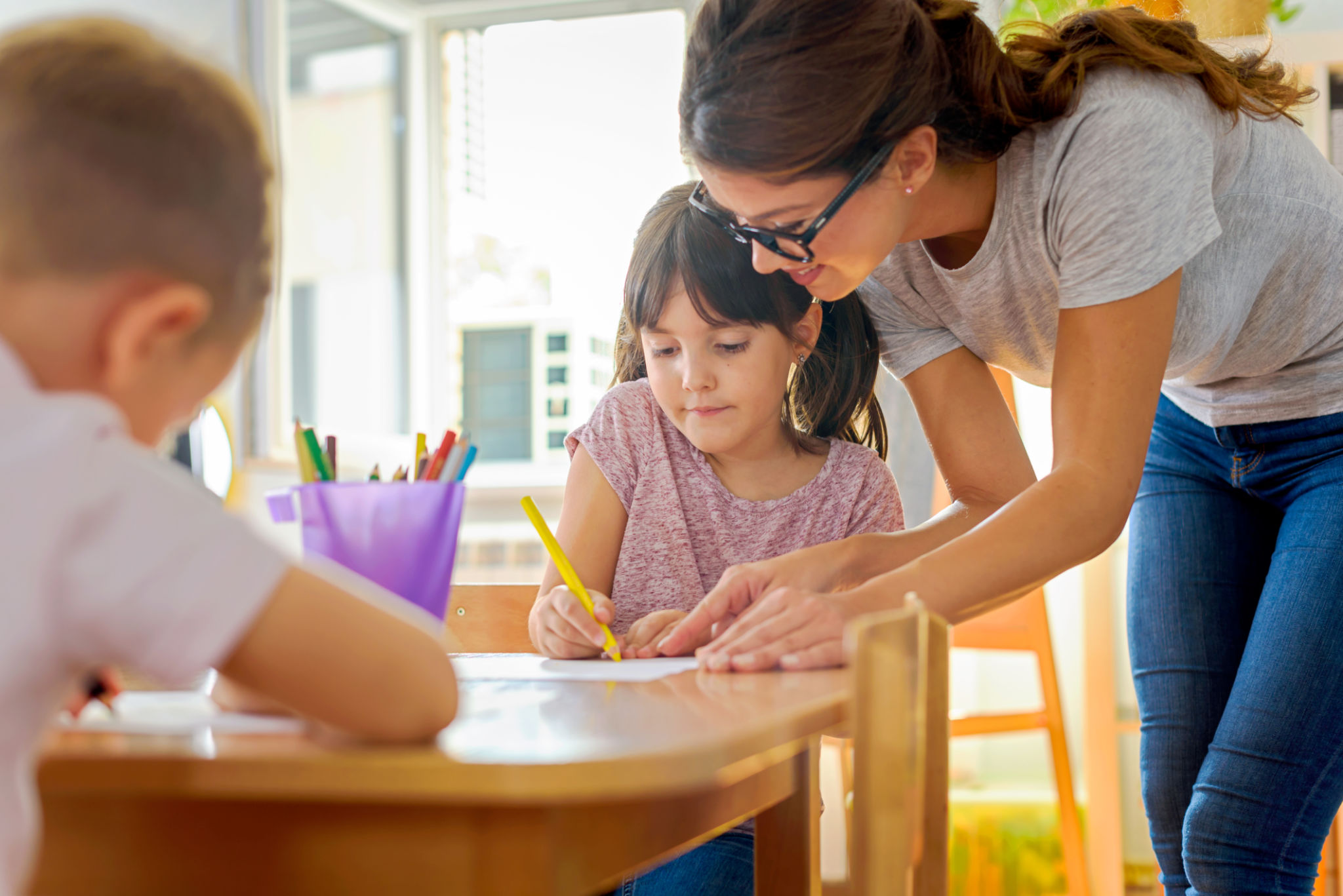 Children drawing with smiling preschool teacher assisting them Children drawing with smiling preschool teacher assisting them