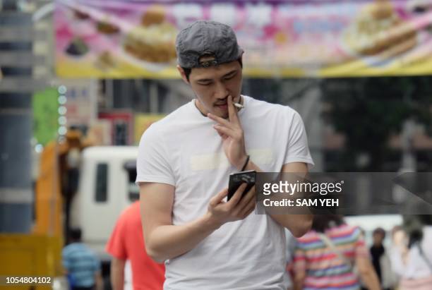 This picture taken on October 24, 2018 shows a man checking his smart phone while smoking in Ximen district in Taipei.