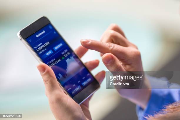 woman buying cryptocurrency through mobile phone app - blockchain crypto stock pictures, royalty-free photos & images