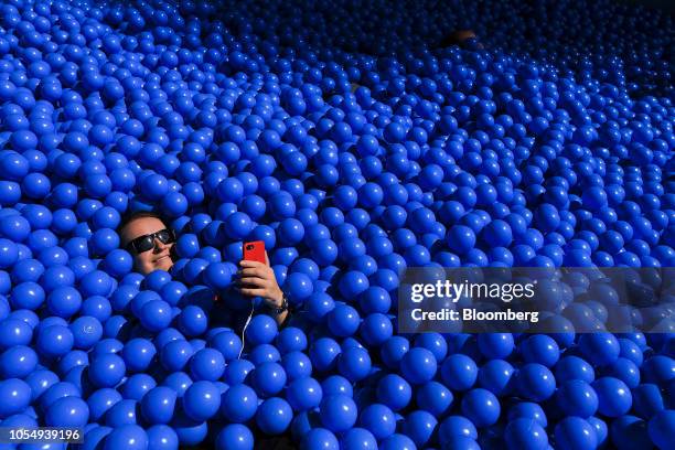 An attendee looks at their smart phone while sitting is a ball pit on the International Business Machines Corp. Stand at the CeBIT 2018 tech fair in...