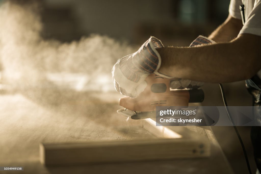 Close up of male construction worker working with sander on a wood plank.