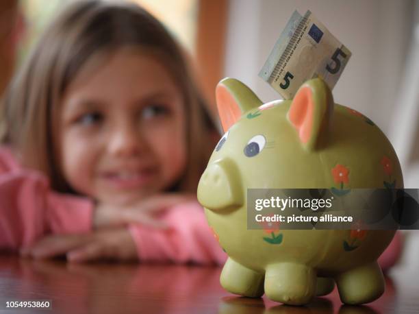 October 2018, Brandenburg, Sieversdorf: Illustration: A girl looks at a 5-euro bill stuck in a piggy bank. 30.10. Is World Savings Day. Photo:...