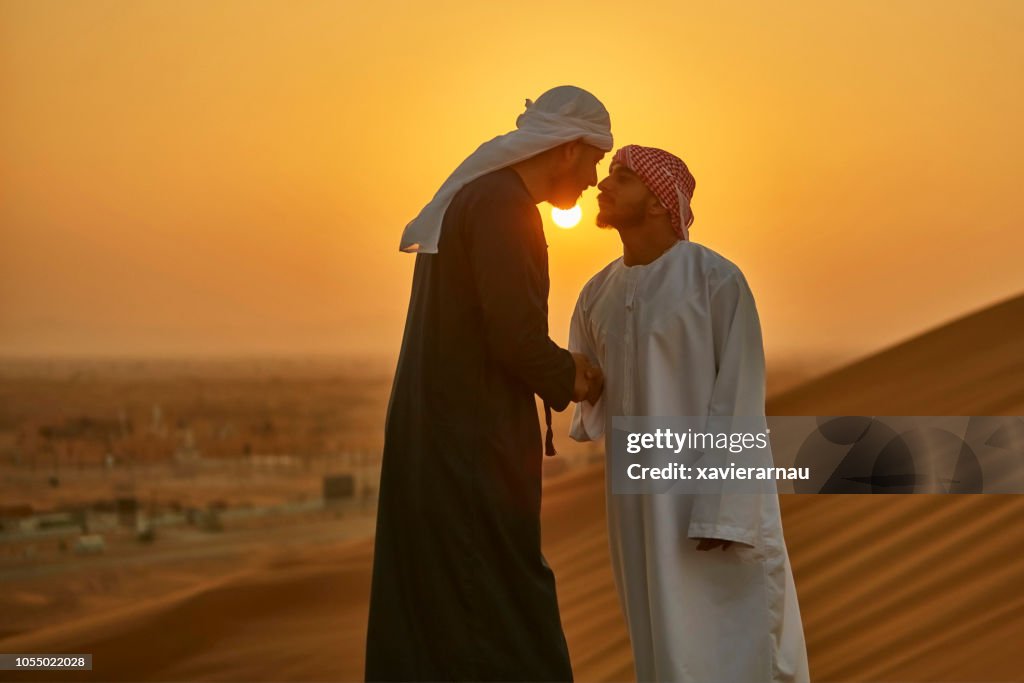 Middle Eastern men greeting in a traditional Arab culture in desert at sunrise