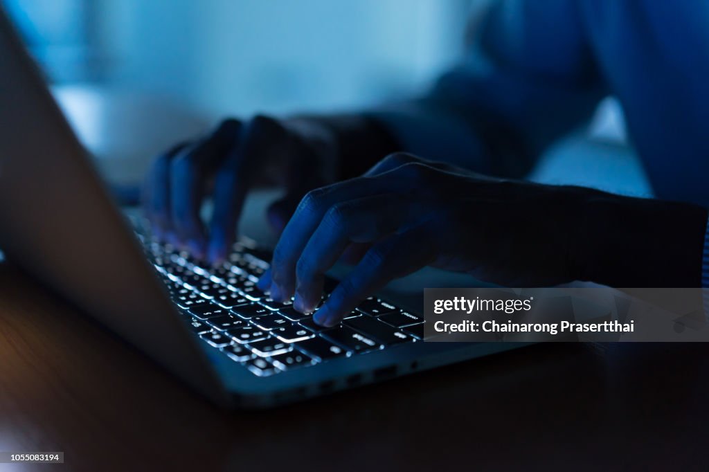 Close up programmer man hand typing on keyboard laptop for register data system or access password at dark operation room , cyber security concept