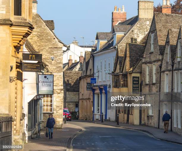 two people walking down a quaint shopping street in cirencester, gloucestershire, the cotswolds on a sunny autumn day - cirencester stock pictures, royalty-free photos & images