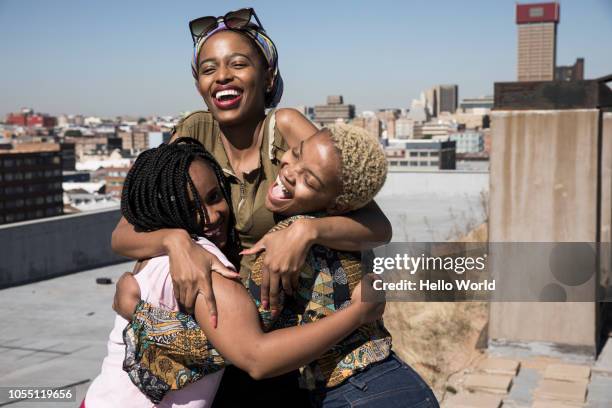 three young women laughing and hugging on a rooftop - sister foto e immagini stock