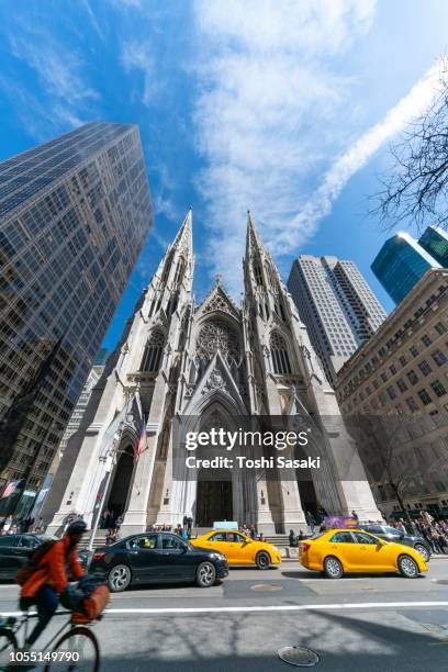 people walk around the st. patrick's cathedral and cars go through fifth avenue among the midtown manhattan skyscrapers at new york ny usa on apr. 22 2018. - american flag church stock pictures, royalty-free photos & images